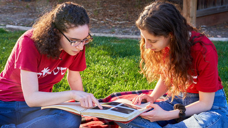 Outdoor photo of two girls looking at a photo book